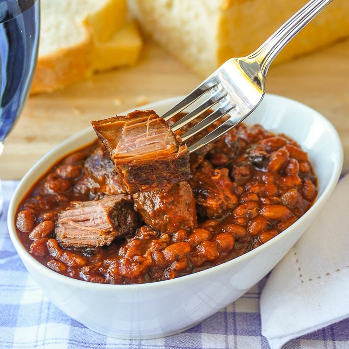 Maple Chipotle Pulled Pork and Beans. in a white bowl with fork holding a chunk of pulled pork.