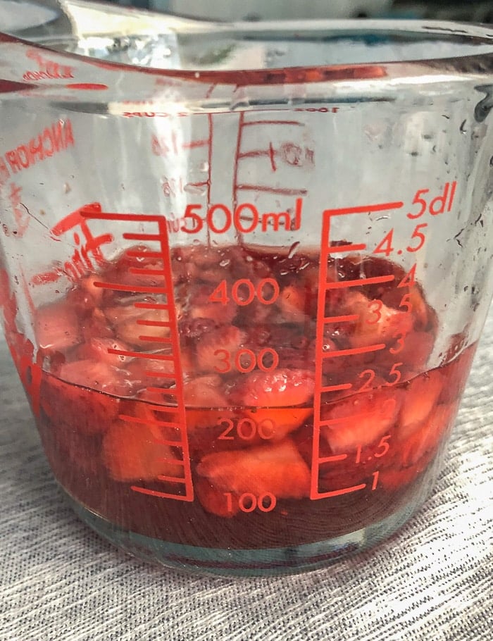 Macerated fresh strawberries in a clear glass measuring cup.