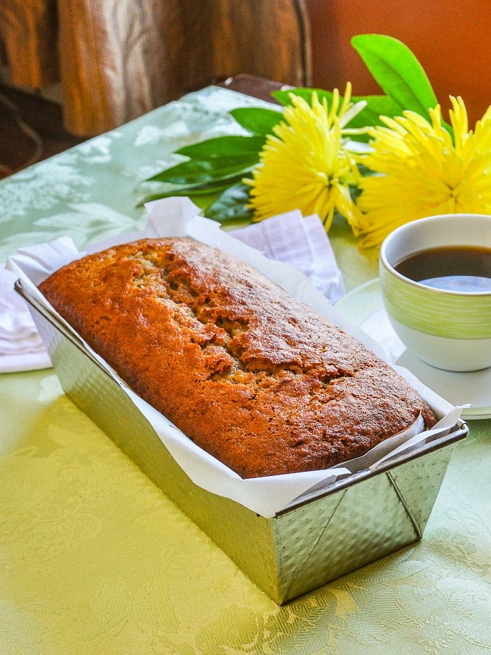 photo of Mango Spice Banana Bread still in the pn with coffee and flowers in the background