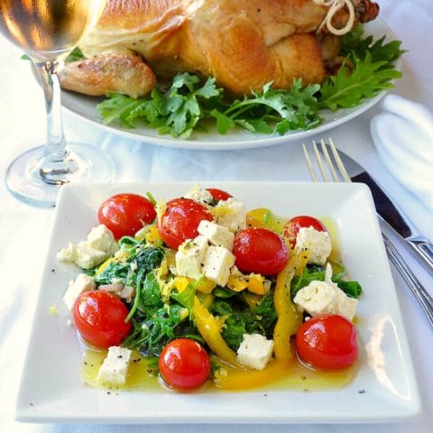 Warm Kale Salad with Lemon & Honey. on a white plate with roast chicken in background