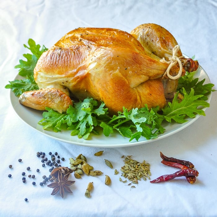 Uncarved Asian Spice Brined Roast Chicken surrounded by the spices used in the recipe