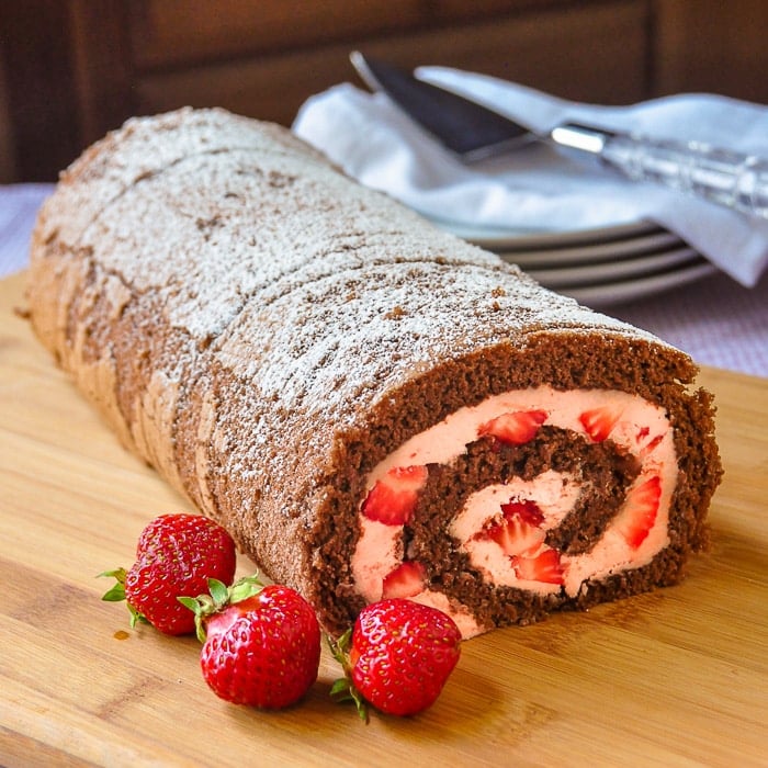 Strawberry Buttercream Chocolate Roll pictured with strawberries on a wooden cutting board