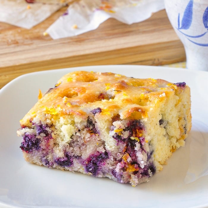 Close up photo of a slice of Blueberry Lemon Drizzle Cake on a square white plate