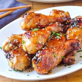 Glazed Sesame Chicken on a white platter garnished with sesame seeds and chives