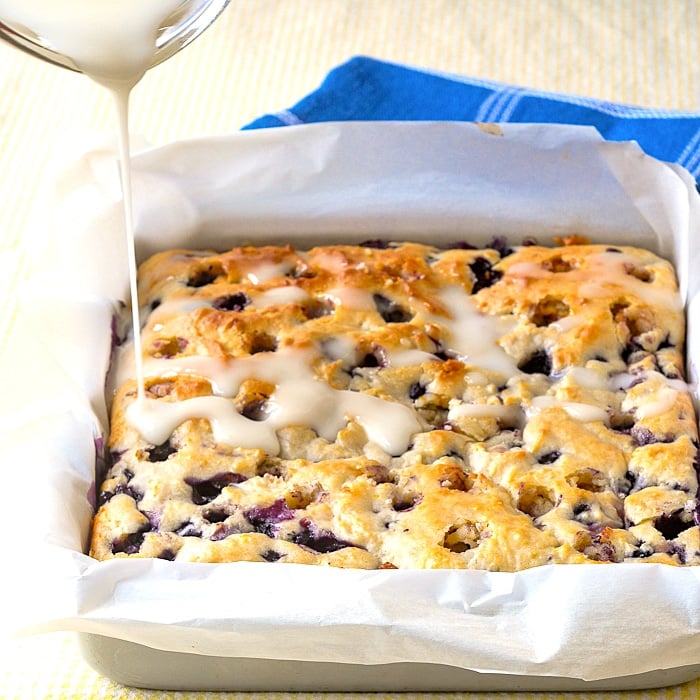 Photo of lemon glaze being poured onto Blueberry Lemon Drizzle Cake