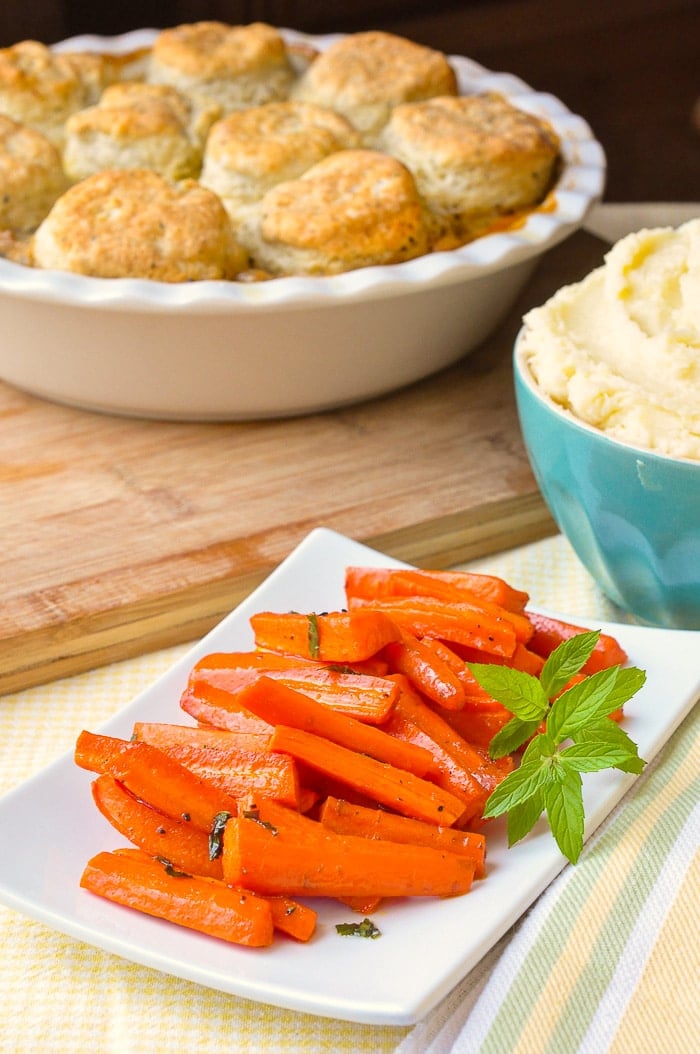 Honey Roasted Carrots with mint shown with mashed potatoes and pot pie in the background