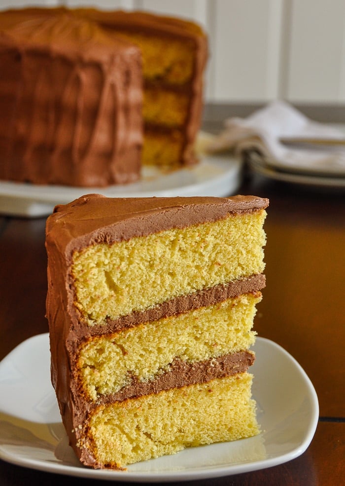 The best Yellow Cake vertical cropped photo of one slice on a white plate with full cake in the background