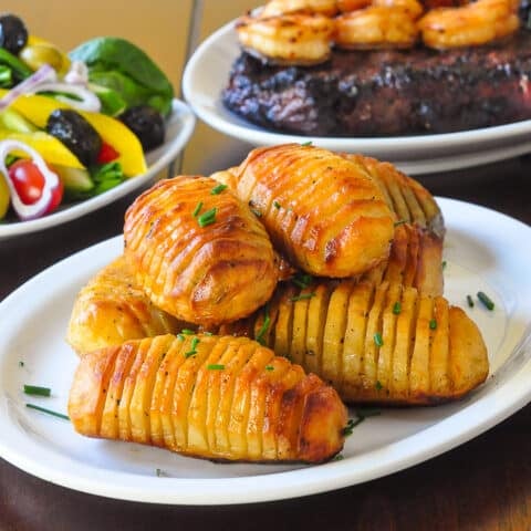Garlic Concertina Potatoes a.k.a. Hasselback Potatoes shown with steak, salad and shrimp in the background