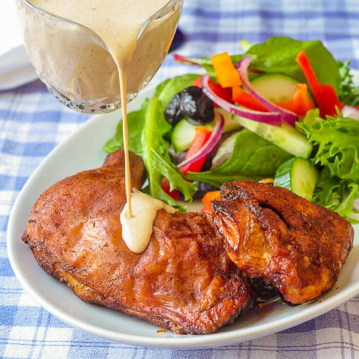 White Barbecue Sauce being poured over a plate of smoked chicken.