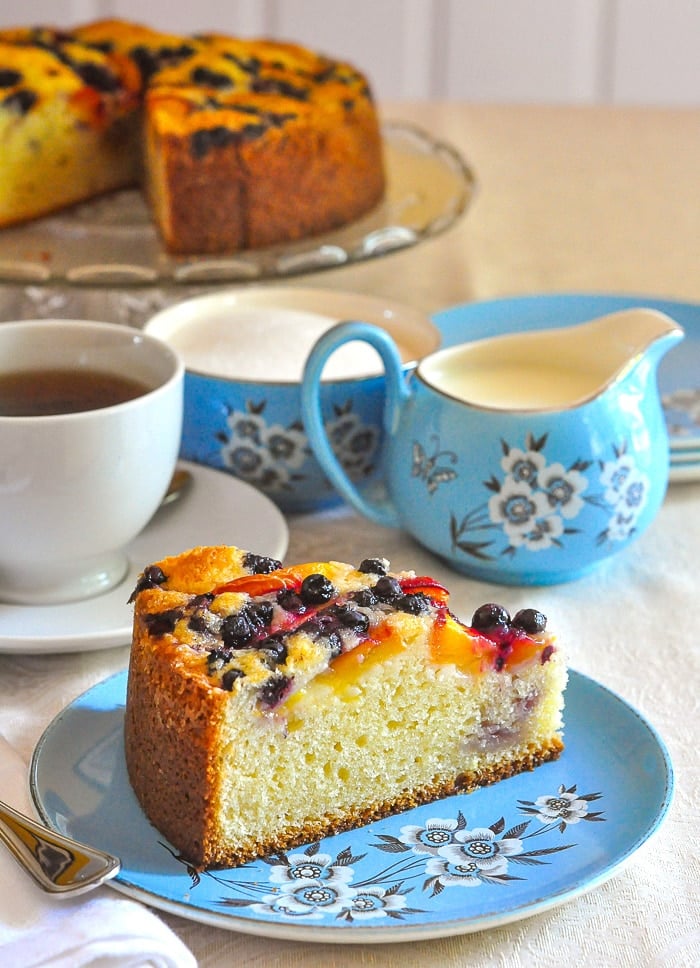 Blueberry Peach Sour Cream Cake photo of a slice and blue tea service with cake in the background.