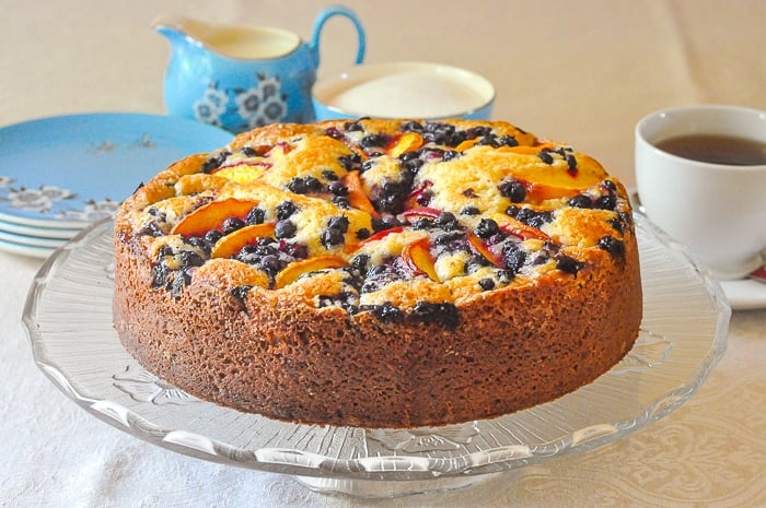 Blueberry Peach Sour Cream Cake wide shhot of entire uncut cake on a glass pedestal