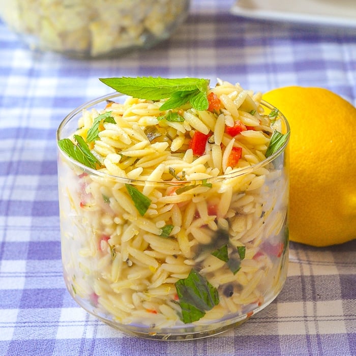 Lemon Mint Orzo Salad in a clear glass serving dish with a whole lemon on the side