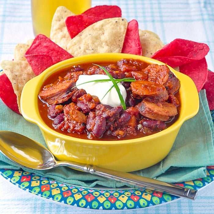 Smoked Sausage Chili in a yellow serving bowl with corn chips on the side