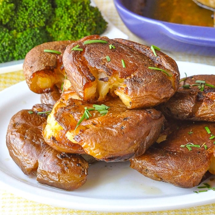 Smash Roasted Potatoes pictured stacked on a white plate