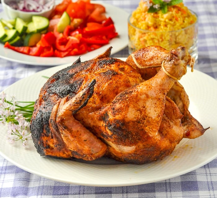 Beer Butt Chicken uncut whole chicken on a white plate with salad in the background