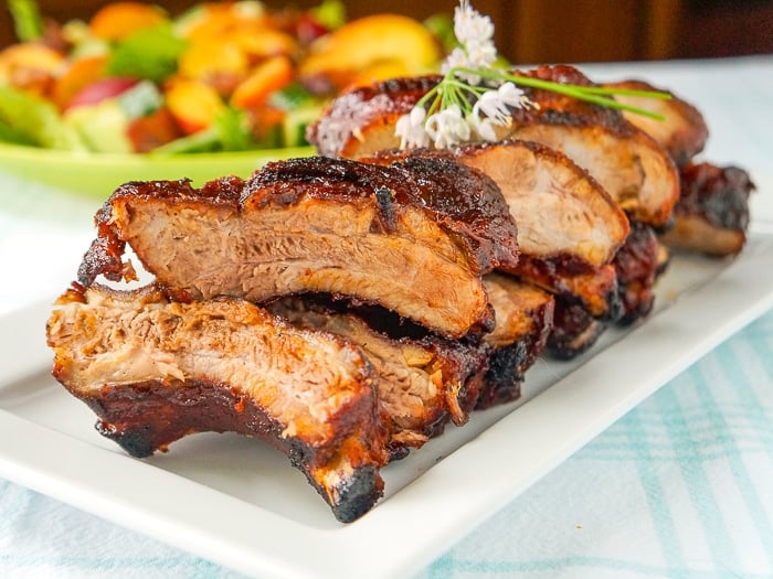 Make Ahead Ribs wide shot of ribs on a serving platter with salad in the background.