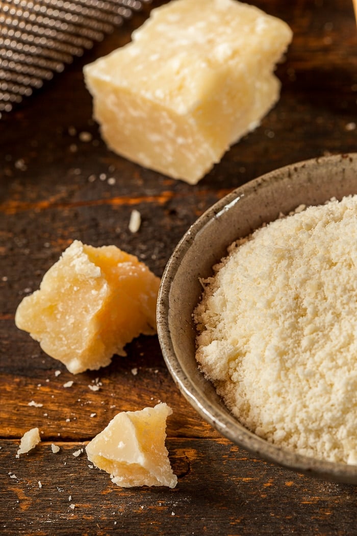 parmigiano reggiano shown in chunks and grated on a wooden background