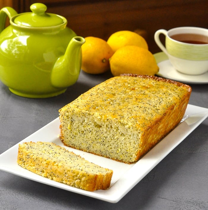 Lemon Poppy Seed Loaf Cake on white serving platter with tea service and fresh lemons in background