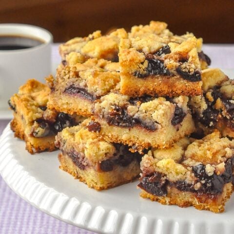 Cherry Almond Squares shown stacked on a white pedestal with coffee in the background