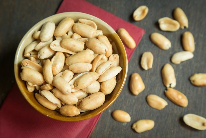 Roasted peeled peanuts in rustic bowl on wooden background (focus on peanut in bowl)