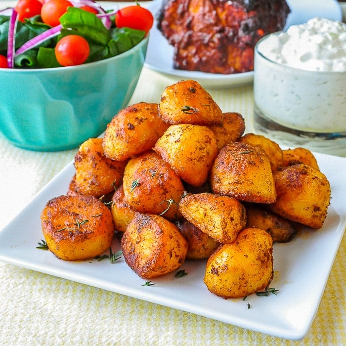 Smoked Paprika Roasted Potatoes wide shot on white serving platter with salad and tzatziki in the background