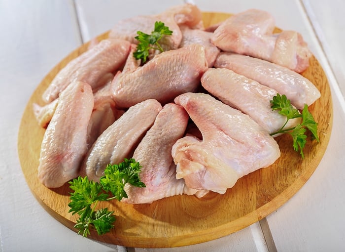 Stock photo of raw chicken wings on chopping board with parsley