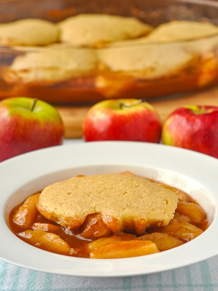 Apple cobbler photo of a single serving with apples and baking dish in background