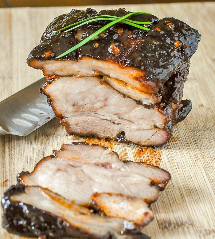 Asian Glazed Pork Belly being sliced on a wooden cutting board