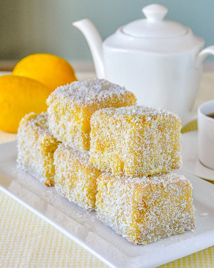 Lemon Lamingtons stacked on white serving plate.