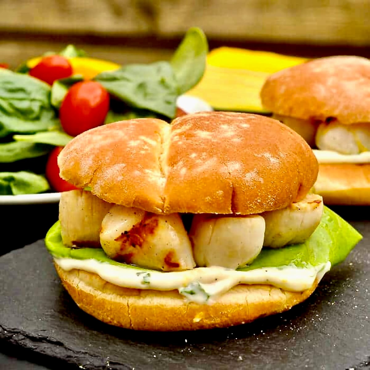 Grilled Scallops Burger with Lemon Basil Mayo shown with salad in thr background for featured image.