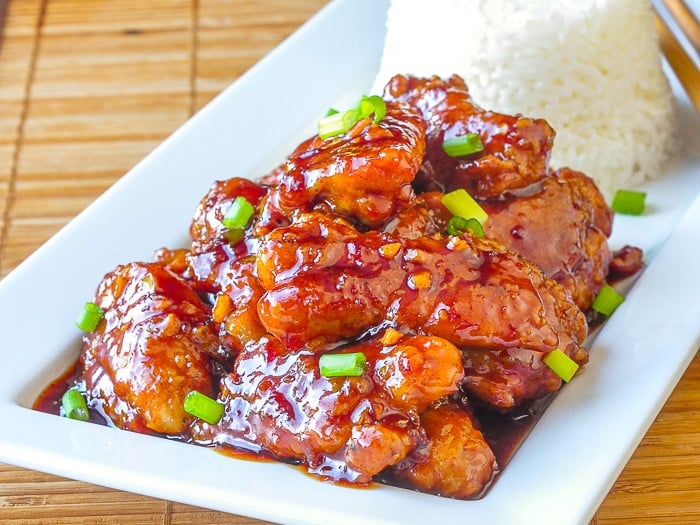 General Tso Chicken on a white serving plate with rice and chopsticks