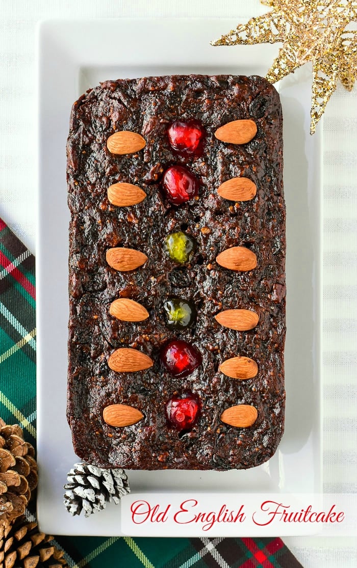 Old English fruitcake overhead photo of baked loaf cake on a rectangular white platter with title text added for Pinterest.