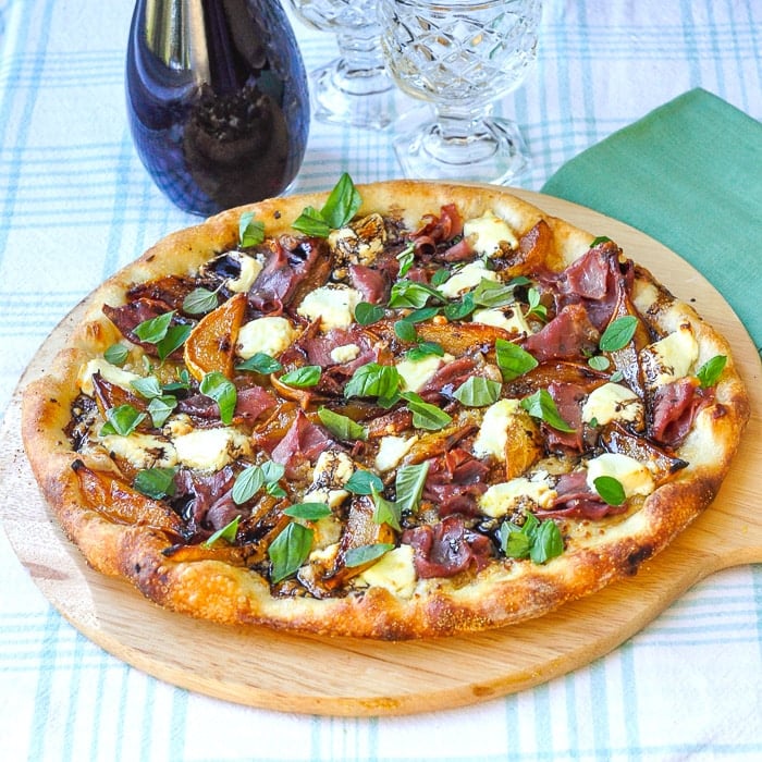 Caramelized Pear Prosciutto Pizza on a wooden peel with wine and glasses in background