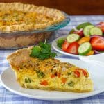 Grilled vegetable quiche, featured square image of slice on a plate with side salad in the background.