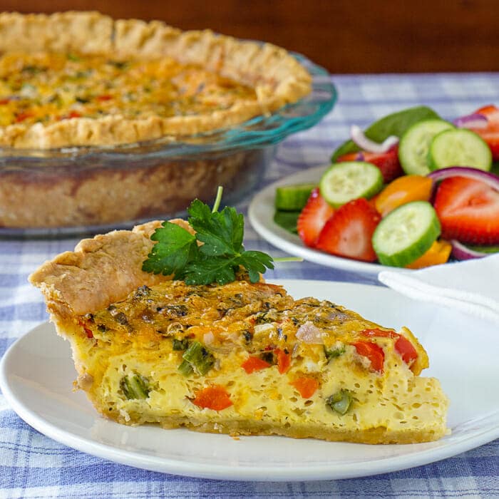 Grilled vegetable quiche, featured square image of slice on a plate with side salad in the background.