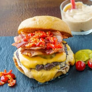 Copycat Smoke Sauce on copycat Smoke Shack Burger pictured with cherry peppers on a slate plate.