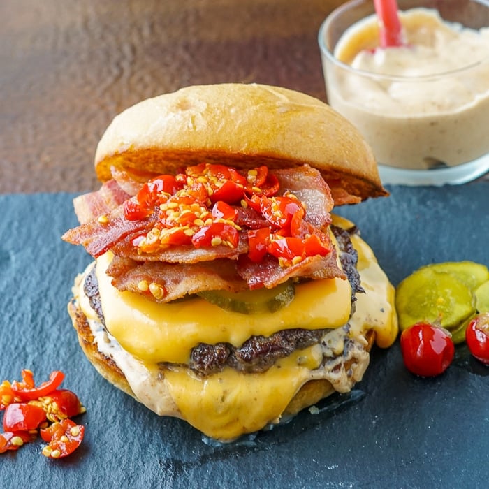 Copycat Smoke Sauce on copycat Smoke Shack Burger pictured with cherry peppers on a slate plate.