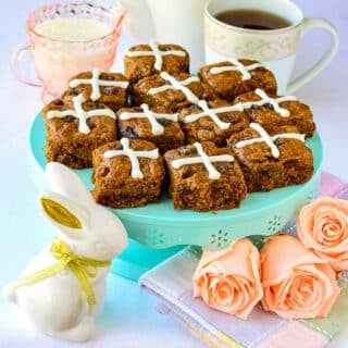 Hot Cross Molasses Raisin Tea Buns shown on a teal pedestal with Easter decorations