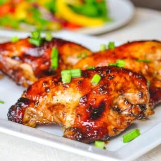 Honey Soy Chicken Breasts shown on white plate with salad in the background.