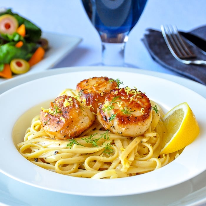 Creamy Lemon Pepper Scallops Linguine wider shot photo of entire bowl with salad in background