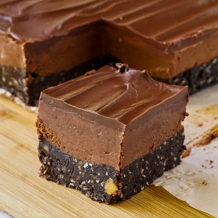 Chocolate Nanaimo Bars close up photo of singe cookie bar on a wooden cutting board