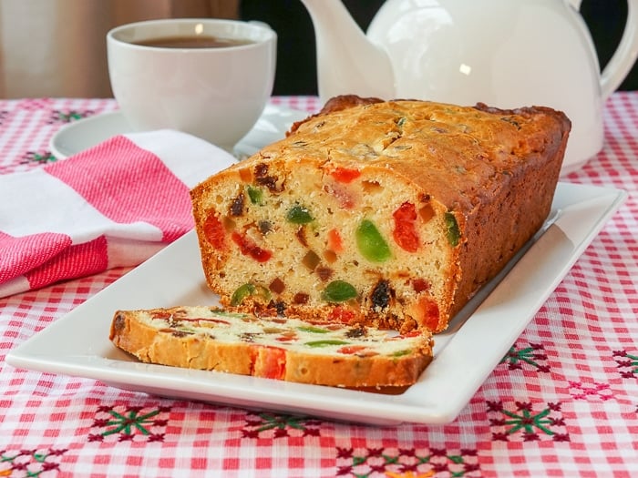 Fruitcake Loaf Cake wide shot photo of entire cake on a white platter with tea in background