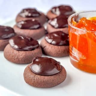 Sachertorte Cookies on a white plate beside a pot of apricot jam.