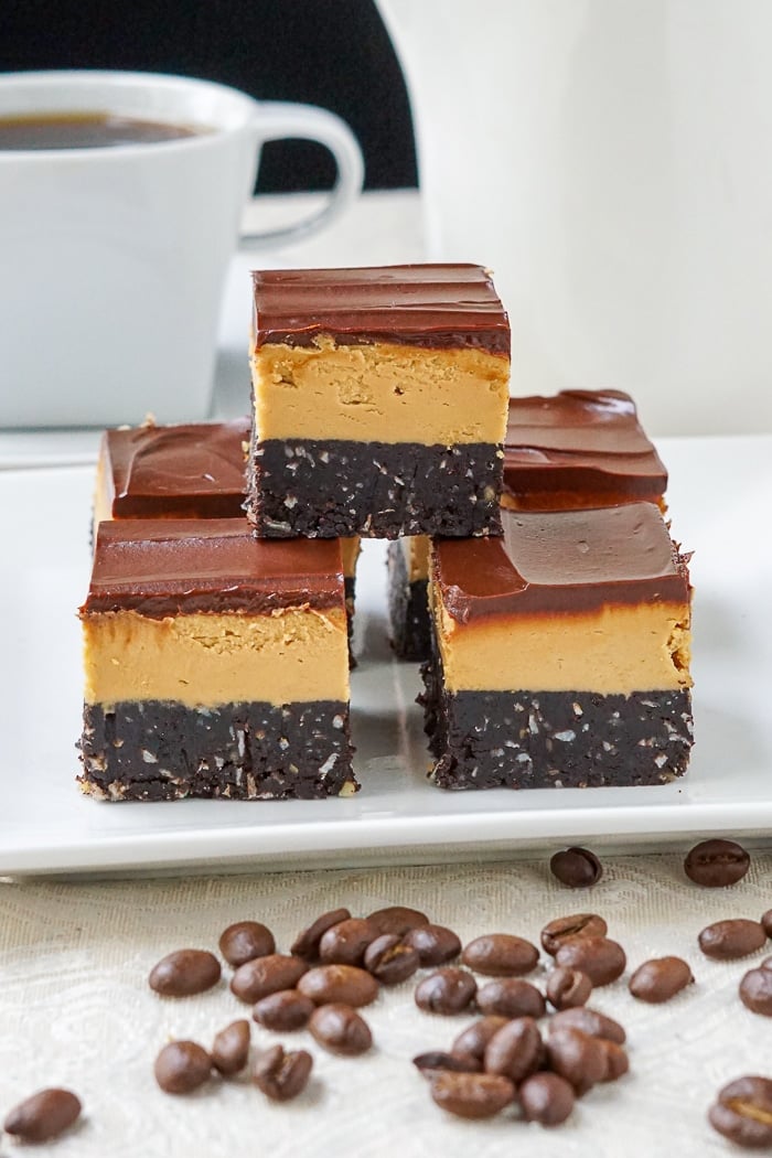 Cappuccino Nanaimo Bars onn a white plate with cup of coffee in background