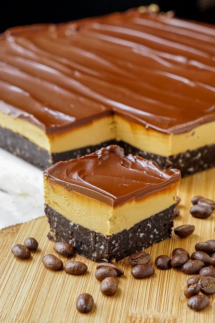 Cappuccino Nanaimo Bars with coffee beans on a wooden cutting board vertical image