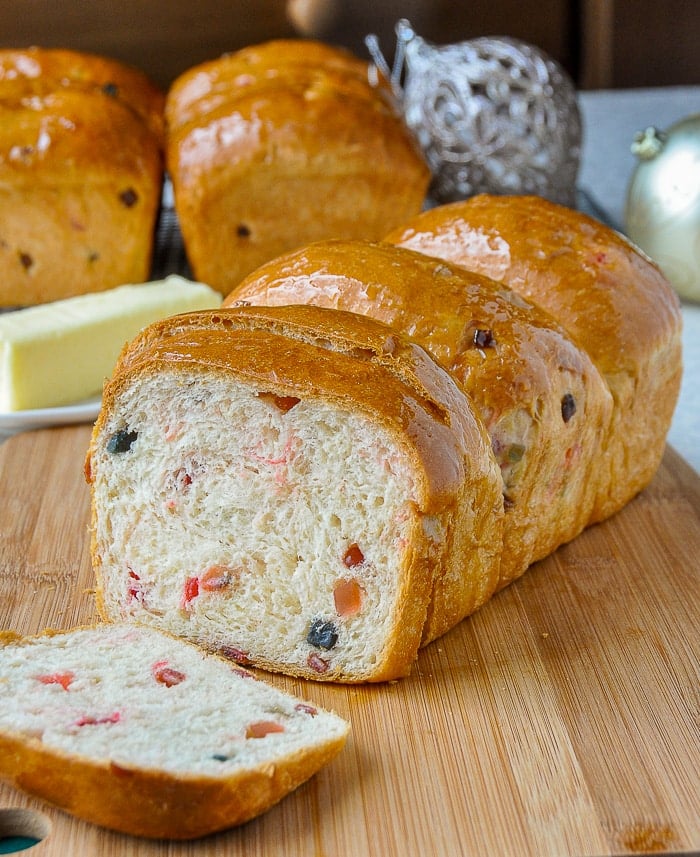 Christmas Fruit Bread shown being sliced with Christmas decorations and other loaves in the background