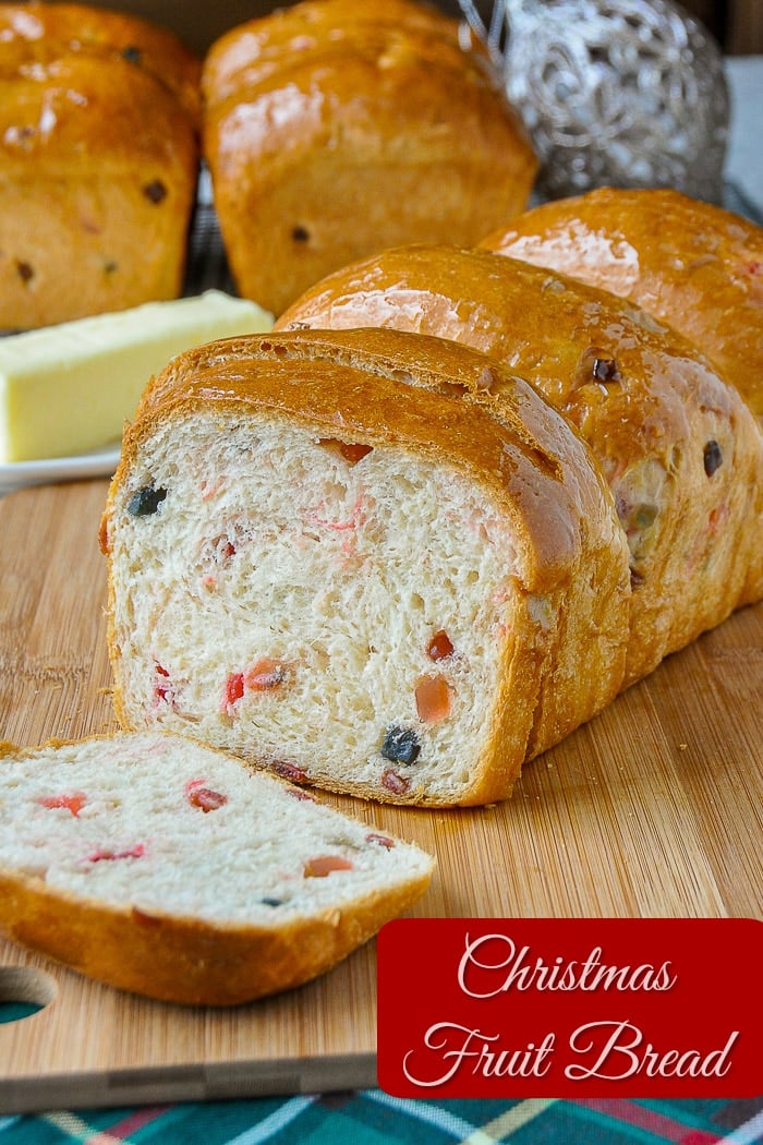 Christmas fruit bread being sliced on a wooden cutting board with title text added for Pinterest