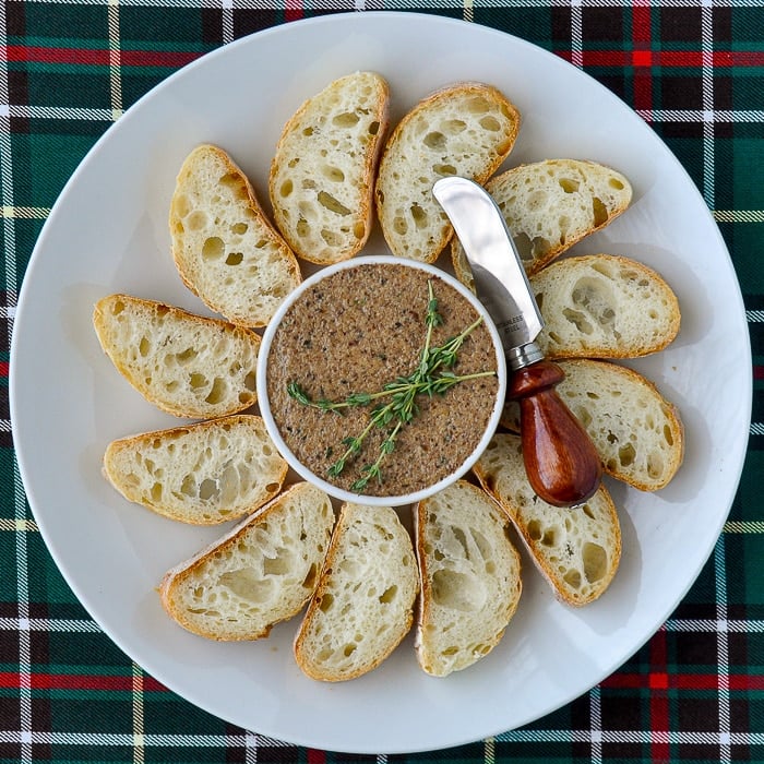 Mushroom Pâté with thyme sprigs garnish on a white platter with sliced baguette