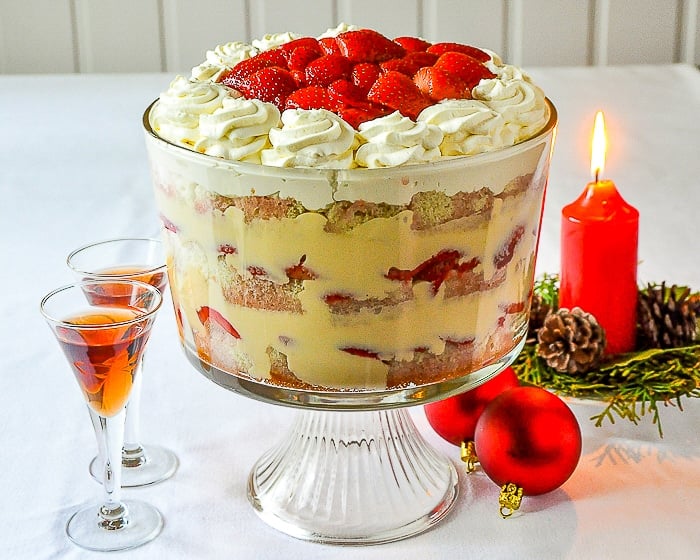 Strawberries and Cream Sherry Trifle in a clear glass bowl surrounded by glasses of sherry, a red lit candle and red christmas tree decorations-1