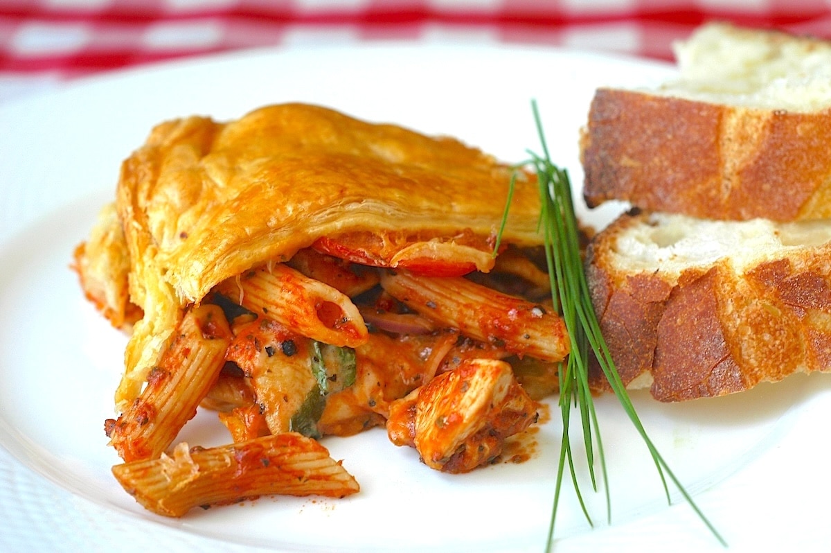 Wide shot photo of Chicken Penne Timpano on a white plate with sliced sourdough bread